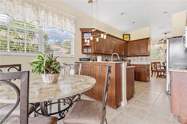3471 Ballybridge Cir Unit 202, Bonita Springs, FL 34134 - kitchen with a peninsula, brown cabinets, decorative backsplash, light tile patterned floors, and pendant lighting