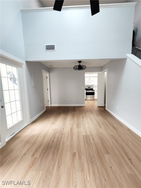 unfurnished living room featuring light wood finished floors, baseboards, ceiling fan, and a high ceiling