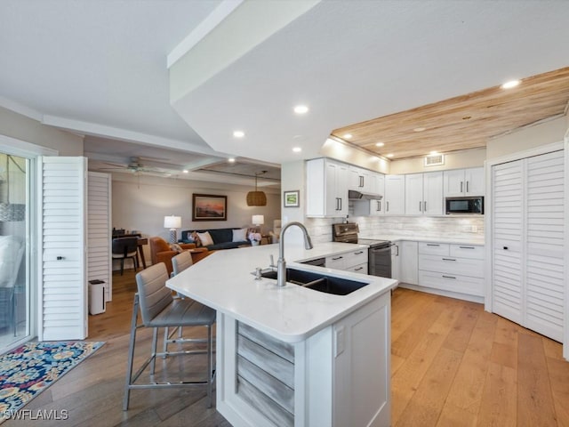 kitchen featuring stainless steel electric stove, a sink, a peninsula, black microwave, and open floor plan