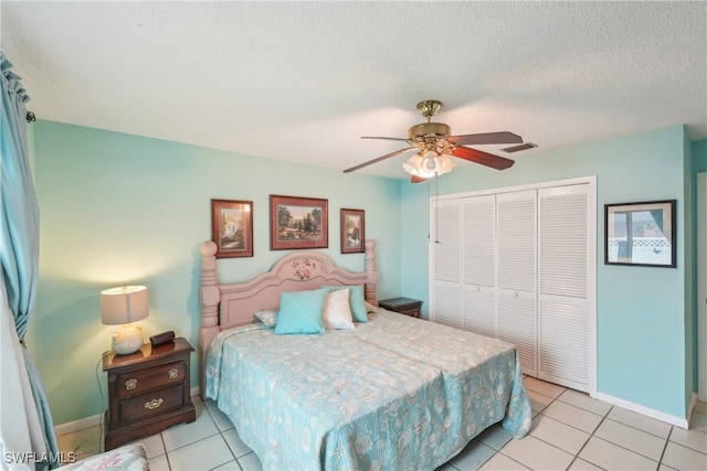 bedroom with a closet, light tile patterned flooring, a ceiling fan, baseboards, and a textured ceiling