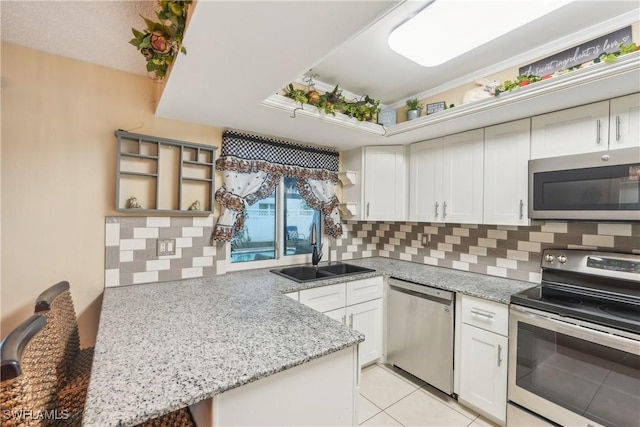 kitchen featuring stainless steel appliances, a sink, open shelves, tasteful backsplash, and a peninsula