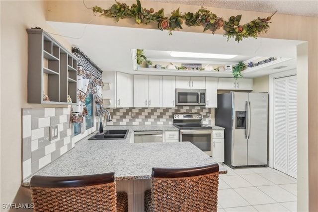 kitchen with appliances with stainless steel finishes, a sink, decorative backsplash, a peninsula, and a kitchen breakfast bar