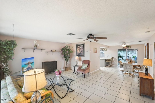 living room with a ceiling fan, a textured ceiling, light tile patterned floors, and baseboards