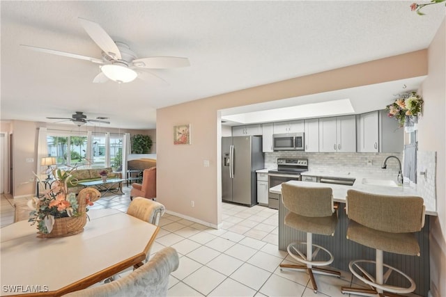 kitchen with stainless steel appliances, a sink, decorative backsplash, light countertops, and a peninsula