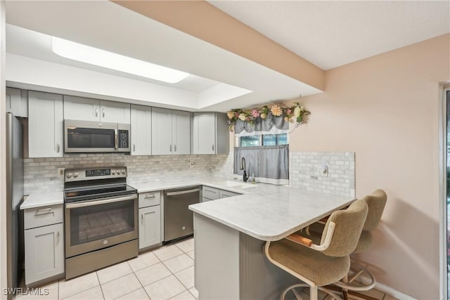 kitchen with appliances with stainless steel finishes, gray cabinetry, a peninsula, and light countertops