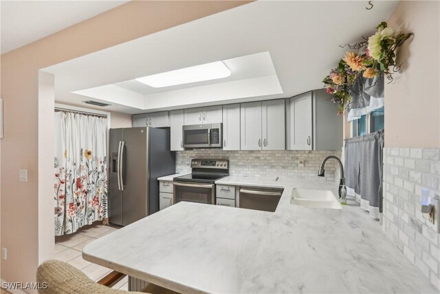 kitchen with appliances with stainless steel finishes, a sink, a raised ceiling, light countertops, and gray cabinets