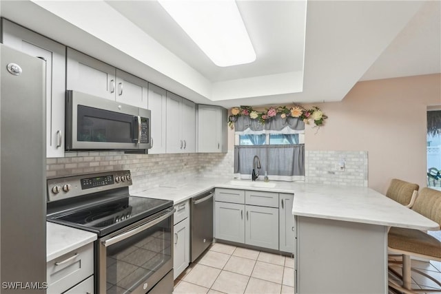 kitchen featuring appliances with stainless steel finishes, a peninsula, a sink, a breakfast bar area, and gray cabinetry