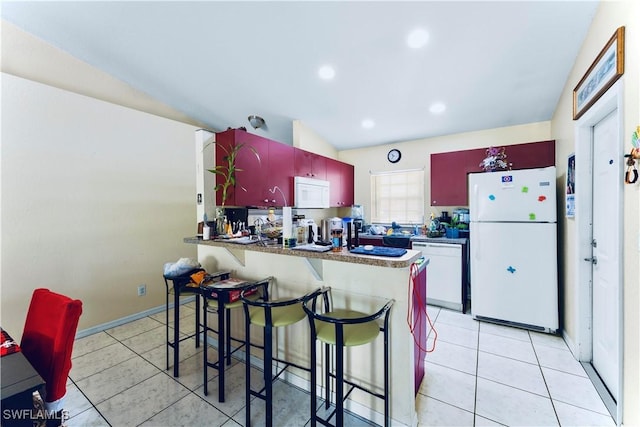869/871 Eisenhower Blvd, Lehigh Acres, FL 33974 - kitchen with white appliances, light tile patterned floors, a peninsula, a breakfast bar area, and dark countertops
