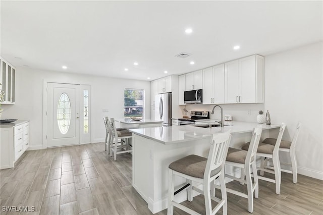 kitchen featuring appliances with stainless steel finishes, a sink, light countertops, a breakfast bar area, and light wood-type flooring