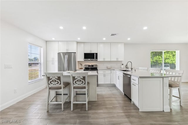 kitchen featuring stainless steel appliances, a sink, a kitchen bar, white cabinetry, and a kitchen island