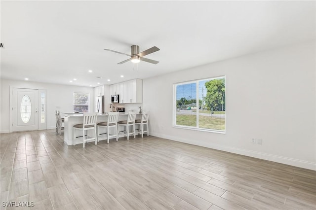 living room with healthy amount of natural light, ceiling fan, light wood-style floors, baseboards, and recessed lighting