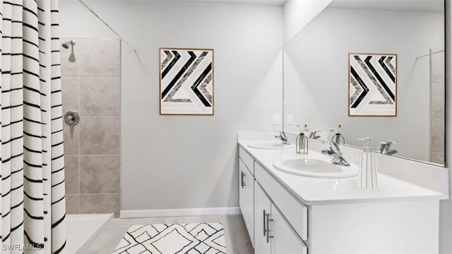bathroom with a tile shower, double vanity, and baseboards