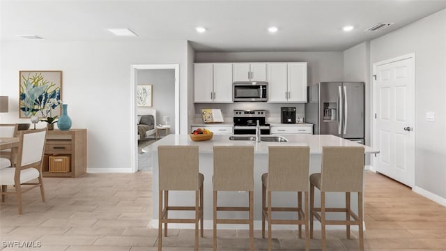 kitchen with stainless steel appliances, recessed lighting, a breakfast bar area, an island with sink, and light wood-style floors