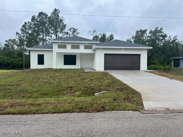 1904 E 11th St, Lehigh Acres, FL 33936 - prairie-style house featuring concrete driveway, stucco siding, a garage, a front yard, and a shingled roof