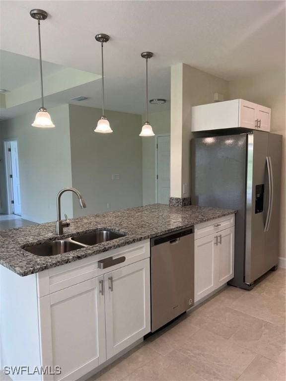 kitchen with appliances with stainless steel finishes, a sink, white cabinets, dark stone countertops, and decorative light fixtures