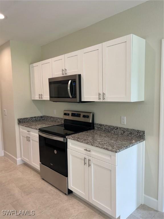 kitchen with appliances with stainless steel finishes, white cabinetry, baseboards, dark stone countertops, and recessed lighting