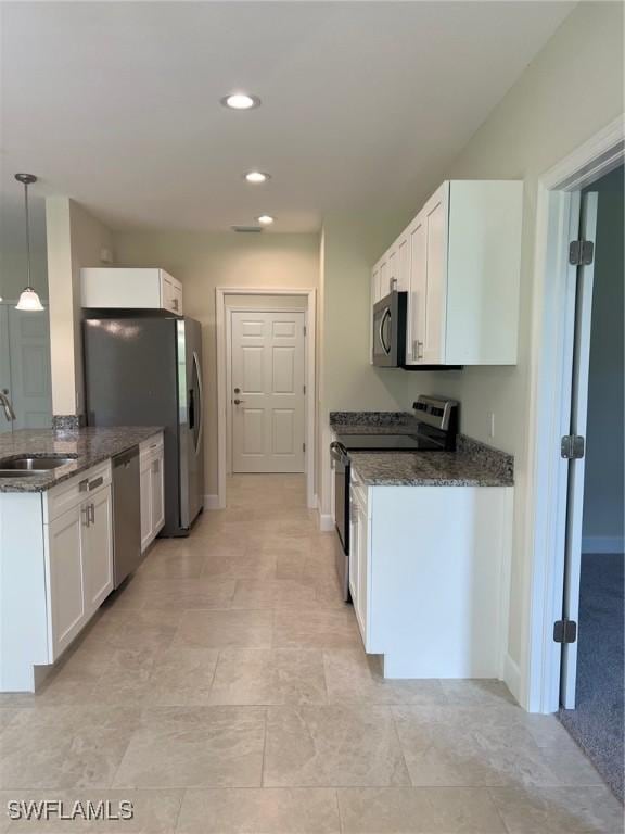 kitchen with stainless steel appliances, a sink, dark stone counters, white cabinetry, and recessed lighting