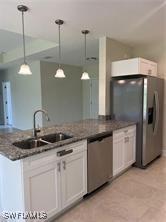 kitchen with stainless steel appliances, white cabinetry, decorative light fixtures, and a sink