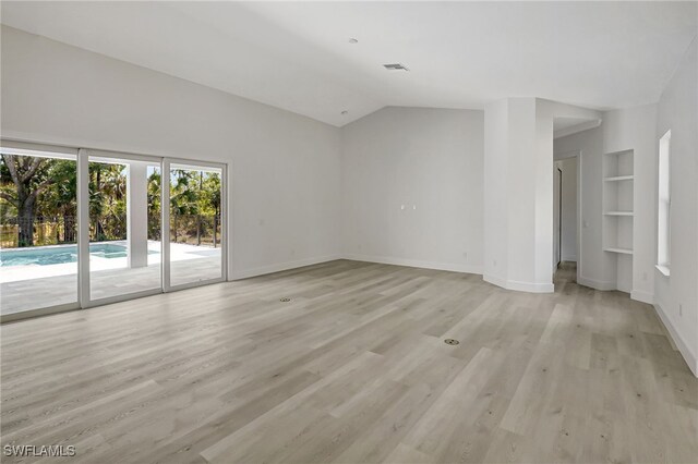 3390 12th Ave SE, Naples, FL 34117 - unfurnished living room with light wood finished floors, baseboards, built in shelves, and lofted ceiling