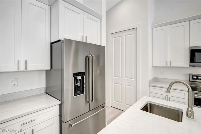 3390 12th Ave SE, Naples, FL 34117 - kitchen with stainless steel appliances, a sink, white cabinetry, and light stone countertops