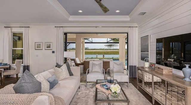 living room featuring wood finished floors, crown molding, a water view, and a tray ceiling