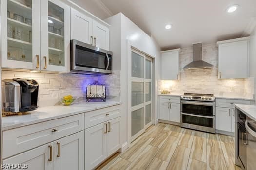 914 Albert Ave, Lehigh Acres, FL 33971 - kitchen featuring wall chimney range hood, stainless steel appliances, tasteful backsplash, light countertops, and white cabinetry