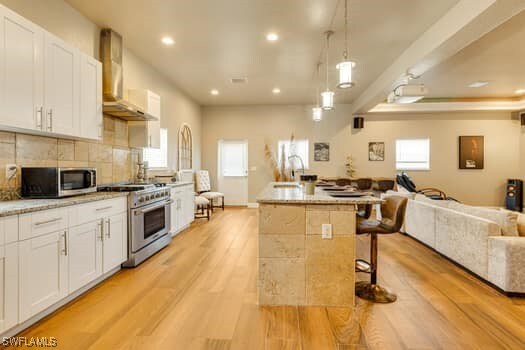 914 Albert Ave, Lehigh Acres, FL 33971 - kitchen featuring appliances with stainless steel finishes, wall chimney exhaust hood, open floor plan, light wood-style flooring, and white cabinetry