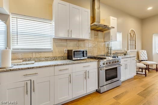 914 Albert Ave, Lehigh Acres, FL 33971 - kitchen featuring stainless steel appliances, wall chimney exhaust hood, light wood-type flooring, white cabinets, and recessed lighting