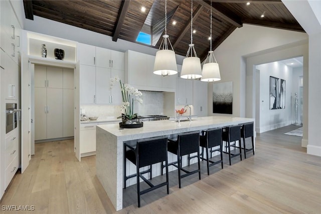 541 Whispering Pine Ct, Naples, FL 34103 - kitchen featuring wooden ceiling, light wood-style flooring, a large island with sink, white cabinetry, and tasteful backsplash
