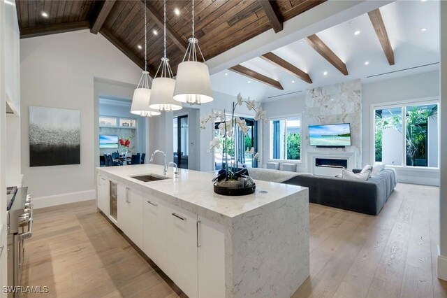 541 Whispering Pine Ct, Naples, FL 34103 - kitchen with a sink, light wood-style flooring, white cabinetry, a kitchen island with sink, and light stone counters