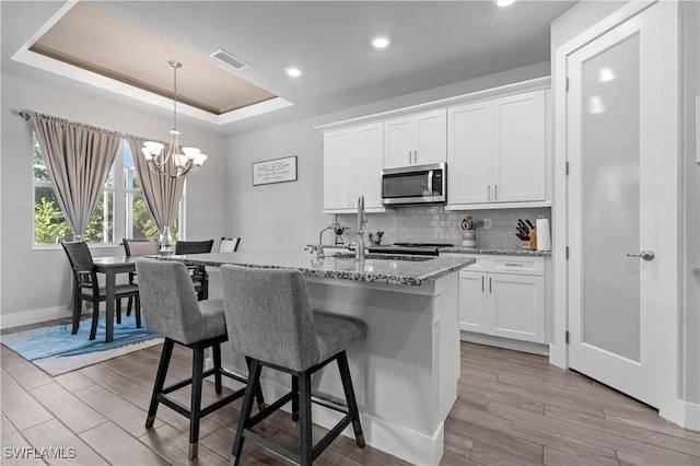 1806 SW 17th St, Cape Coral, FL 33991 - kitchen featuring stainless steel microwave, wood finished floors, backsplash, an island with sink, and a breakfast bar