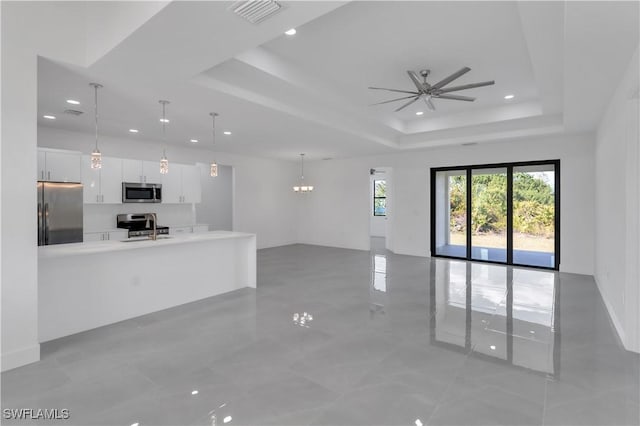 unfurnished living room with a sink, a raised ceiling, a ceiling fan, recessed lighting, and a chandelier