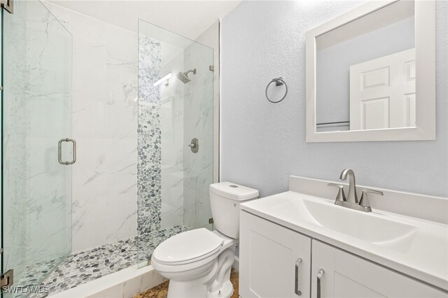 full bathroom with a marble finish shower, toilet, a textured wall, and vanity