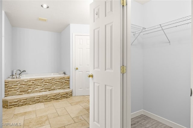 bathroom featuring a bath, a walk in closet, baseboards, and stone finish flooring