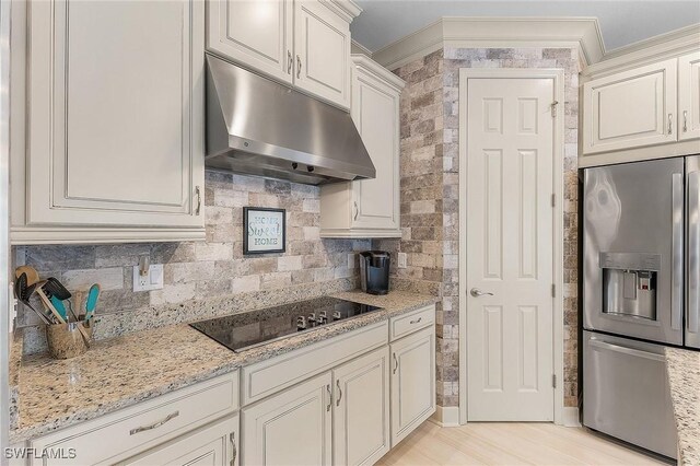 2736 Lambay Ct, Cape Coral, FL 33991 - kitchen with stainless steel fridge, under cabinet range hood, black electric cooktop, light stone countertops, and decorative backsplash