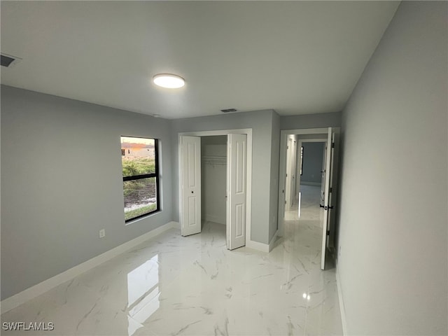 unfurnished bedroom with baseboards, light marble finish floors, and a closet