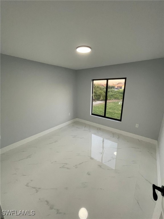 spare room featuring marble finish flooring and baseboards