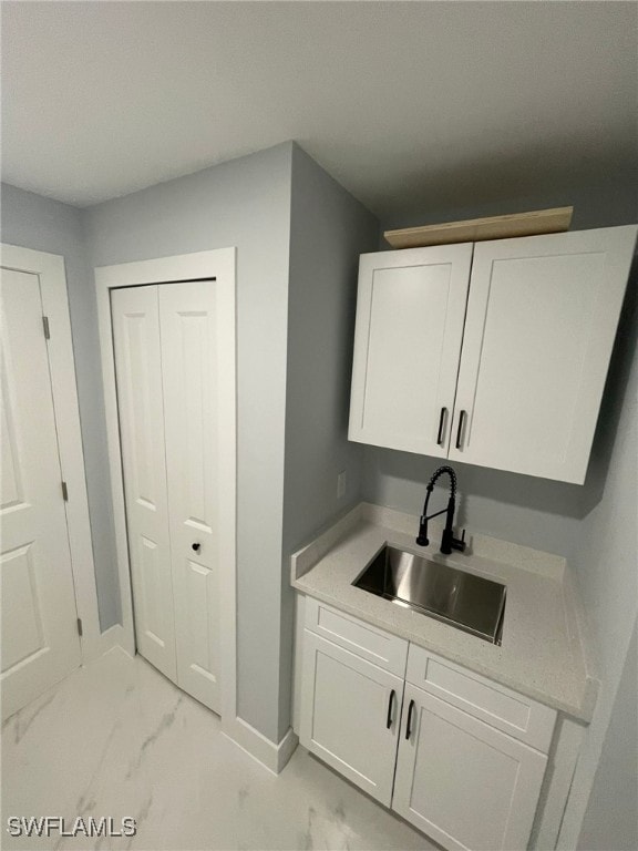 laundry room featuring a sink, light marble finish flooring, and baseboards