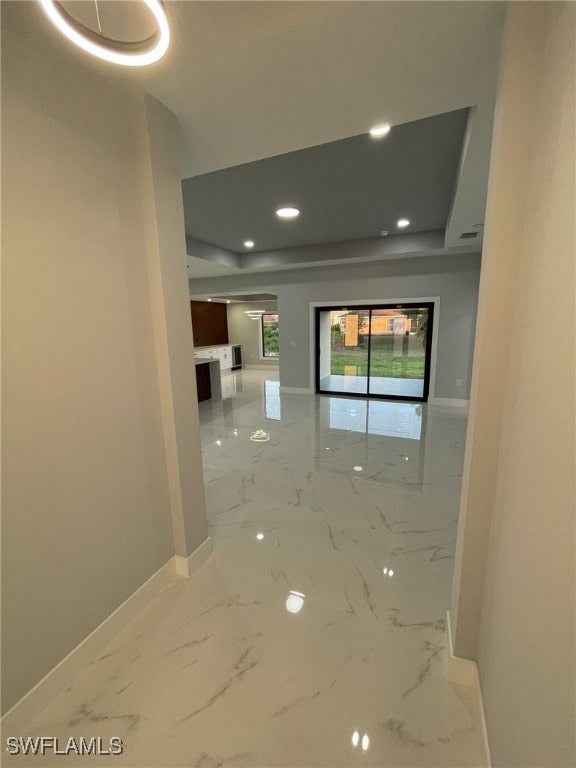 corridor featuring baseboards, marble finish floors, recessed lighting, and a tray ceiling