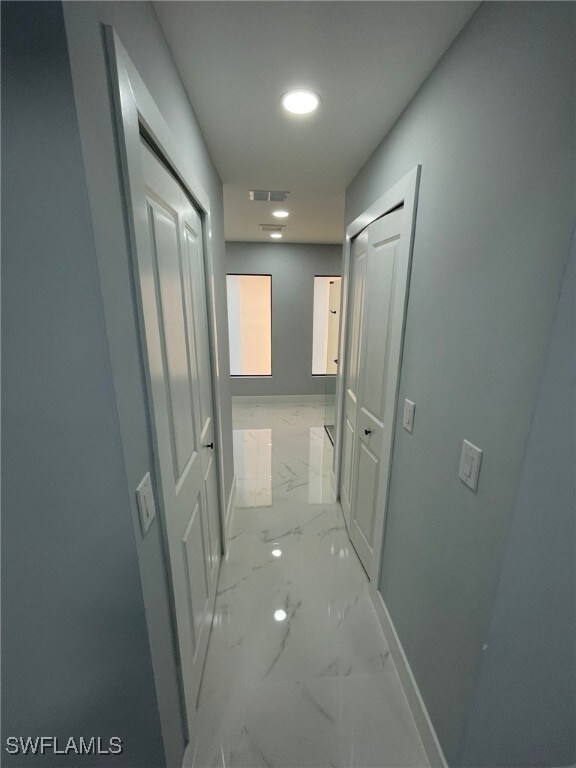 hallway featuring light marble finish floors and baseboards