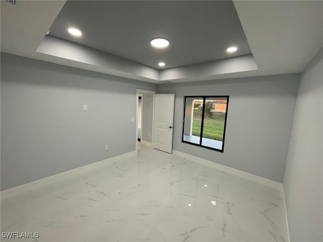 empty room featuring a raised ceiling, baseboards, recessed lighting, and light marble finish flooring