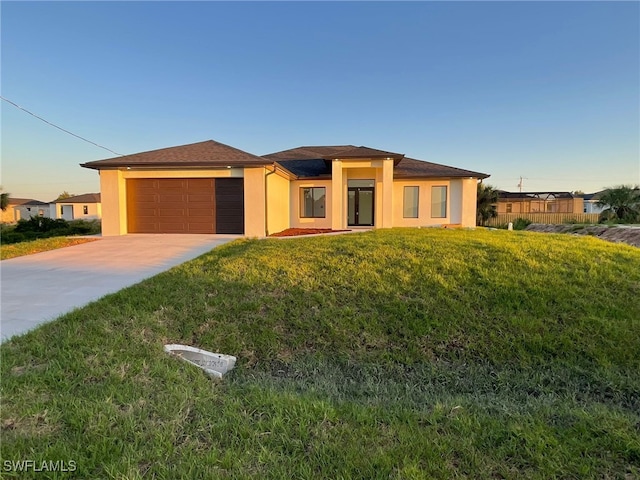 prairie-style house featuring a garage, a front lawn, stucco siding, and concrete driveway