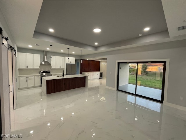 kitchen with wall chimney range hood, stainless steel appliances, a barn door, light marble finish floors, and a tray ceiling