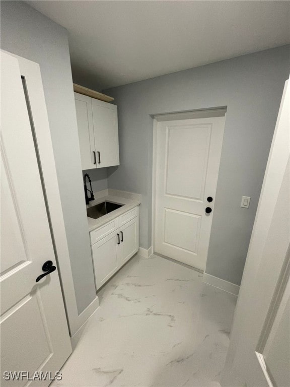 laundry area featuring a sink, light marble finish flooring, and baseboards