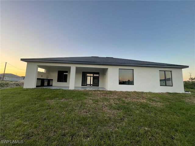 rear view of house featuring stucco siding, a yard, and a patio area
