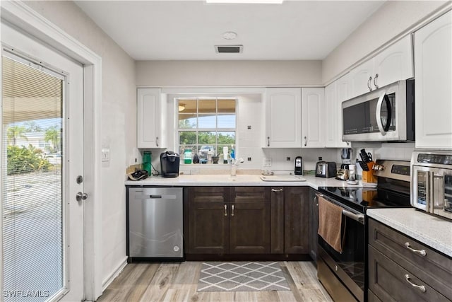 12206 Boat Shell Dr, Matlacha Isles, FL 33991 - kitchen featuring appliances with stainless steel finishes, white cabinets, light wood-type flooring, and dark brown cabinetry