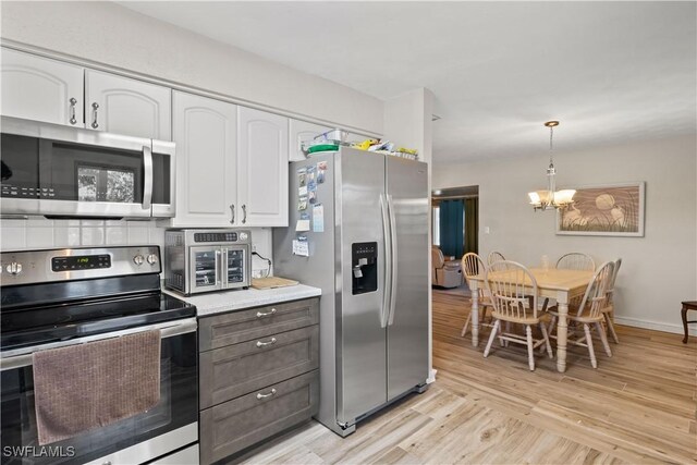 12206 Boat Shell Dr, Matlacha Isles, FL 33991 - kitchen featuring stainless steel appliances, white cabinetry, a chandelier, light wood-type flooring, and light countertops