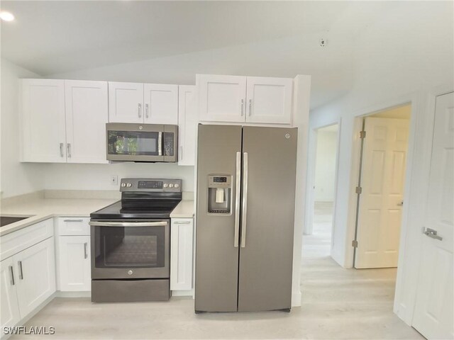 687 Grove Dr, Naples, FL 34120 - kitchen with appliances with stainless steel finishes, light wood-type flooring, white cabinets, lofted ceiling, and light countertops