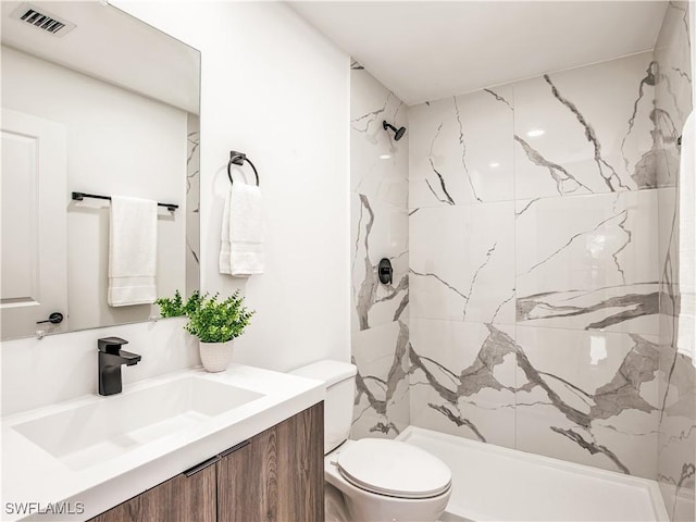 bathroom with toilet, a marble finish shower, and vanity