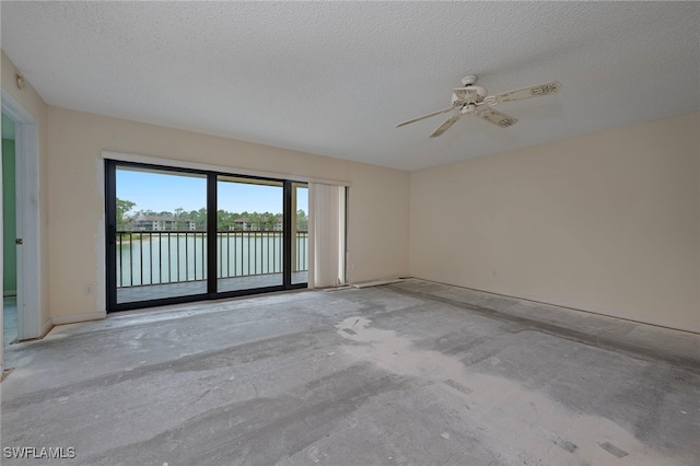 empty room featuring concrete flooring, a ceiling fan, a textured ceiling, and a water view